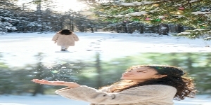 两宫格艺术感写真图，横向两宫格，场景为冬日落雪森林，色调呈冷白与浅绿渐变，松枝挂雪，地面铺薄雪，空中飘彩色雪粒（绿 / 金 / 粉），阳光透过树枝洒下光斑。画面主体为穿浅咖毛呢大衣的少女。上图：少女背预览效果