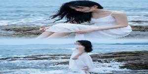 高清旅拍写真，无痕二宫格分镜，上下零缝隙渐变晕染拼接，无实体分割线，整体清冷情绪风格：上半格：年轻东亚女性近景特写（黑长直、白色吊带裙），坐在礁石上低头整理裙摆，背景是翻涌的浅蓝海浪（礁石纹理清晰），预览效果