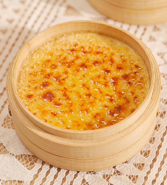 焦糖布丁放在竹制蒸笼里，放置在白色蕾丝餐布上，表面焦糖化，金黄诱人，高清晰度，美食摄影风格，质感细腻，光线柔和