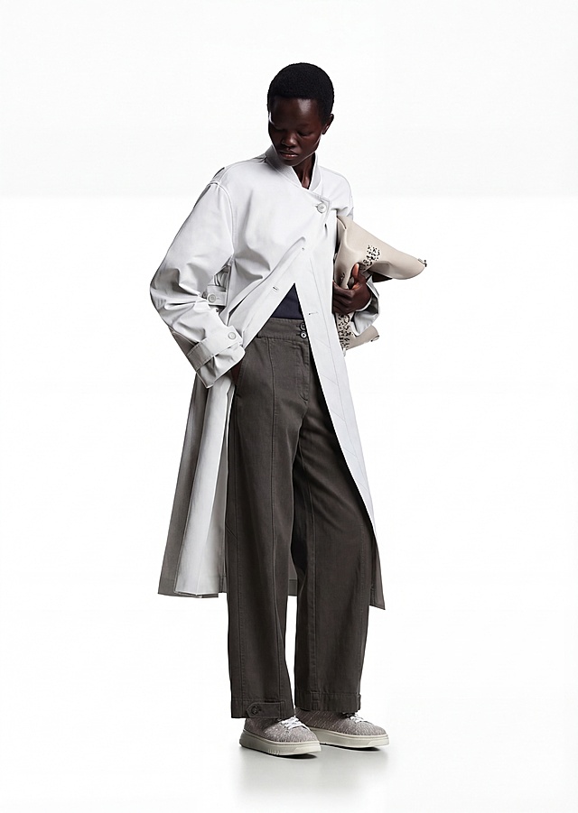 将图中模特所穿的浅卡其色阔腿裤替换为提供的深灰色休闲裤，高度还原这条深灰色裤子的腰部双扣、侧边调节袢、裤腿中线、裤脚按扣等所有细节，保持模特的姿势、上衣、鞋子、包和背景不变，画面整体风格和光影与原图一致，融合自然真实