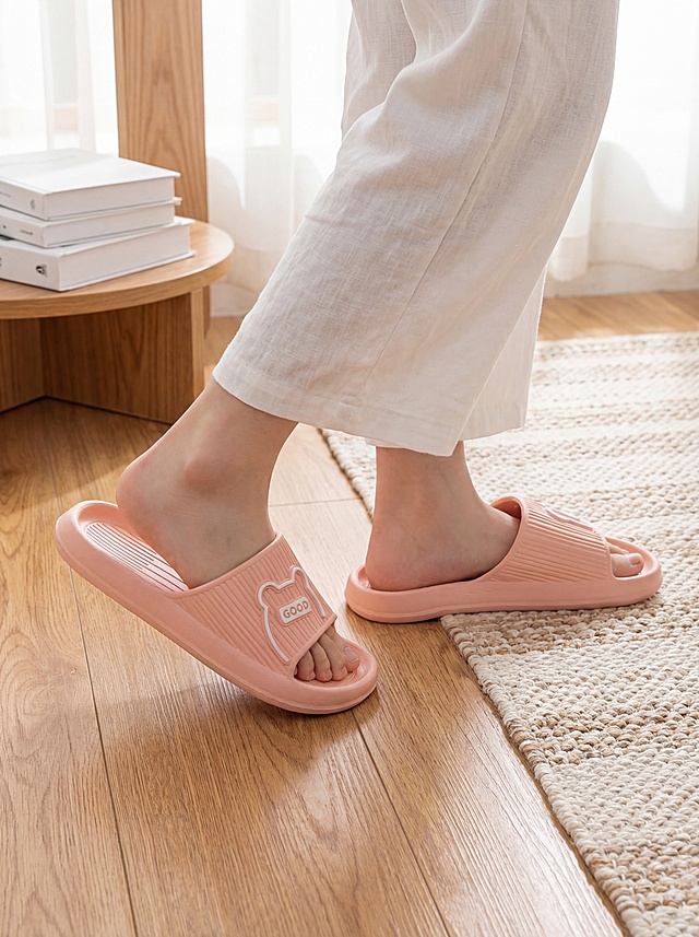 保持原图粉色拖鞋主体外观完全不变，更改背景为居家场景：人物身着白色夏季家居服，刚从地毯走到地板，一只脚踩在浅棕色木质地板另一只脚还在地毯边缘，穿着同款粉色拖鞋，背景左侧有堆叠的白色书籍，整体氛围温馨居家，电商产品摄影风格，主体清晰突出，质感细腻，构图居中偏下，自然光柔和打光，细节写实，色彩还原真实，高清8K分辨率，无水印，姿势：跨步换平面展示拖鞋
