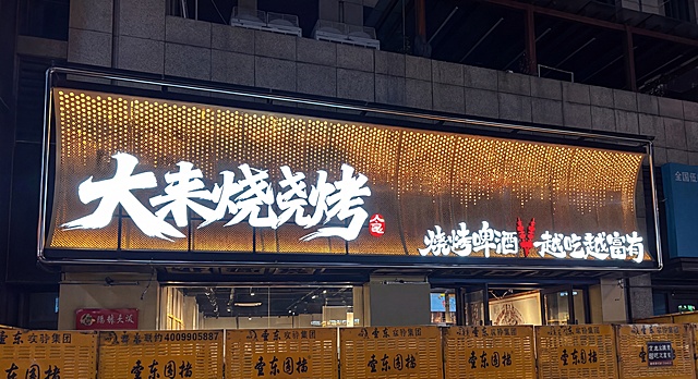 参考实景门头框架，生成大未来烧烤门店门头效果图，黄橙色背景做倾斜折弯金属冲孔板材质，黑色支撑用不锈钢管，文字'大未来烧烤'和'烧烤啤酒 越吃越富有'做成发光字，整体呈现立体感，保留平面设计中的文字内容和排版，放置在实景建筑外框中