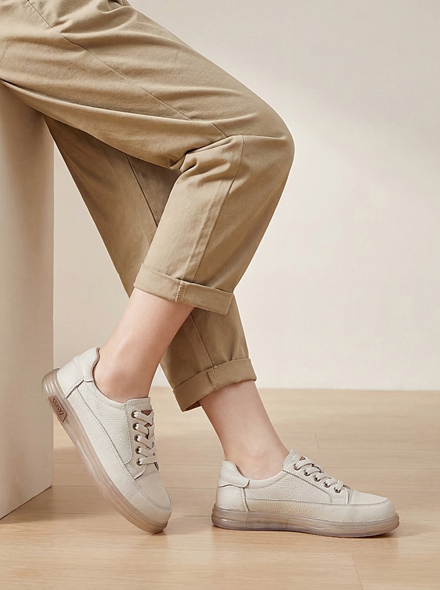 美女模特上脚实拍图，只拍腿部中景镜头，凸出鞋子，显腿长显瘦。模特搭配卡其色休闲裤，穿着这双米白色头层牛皮休闲板鞋，保留原图牛皮皮纹质感，保留鞋子原色，鞋子为纯色没有拼色，保持原有鞋子Logo和结构不变。高清真实的电商详情图，淘宝天猫平台风格，时尚种草氛围感，东亚模特，松弛倚靠姿态，商业高调摄影，柔和漫射光，低饱和度浅色系背景，画面干净通透，凸显鞋子质感。负向提示词：西方面孔、金发、深眼窝、雀斑、杂乱房间、死黑阴影、硬光、高对比度、鞋子变形、Logo扭曲、文字错乱