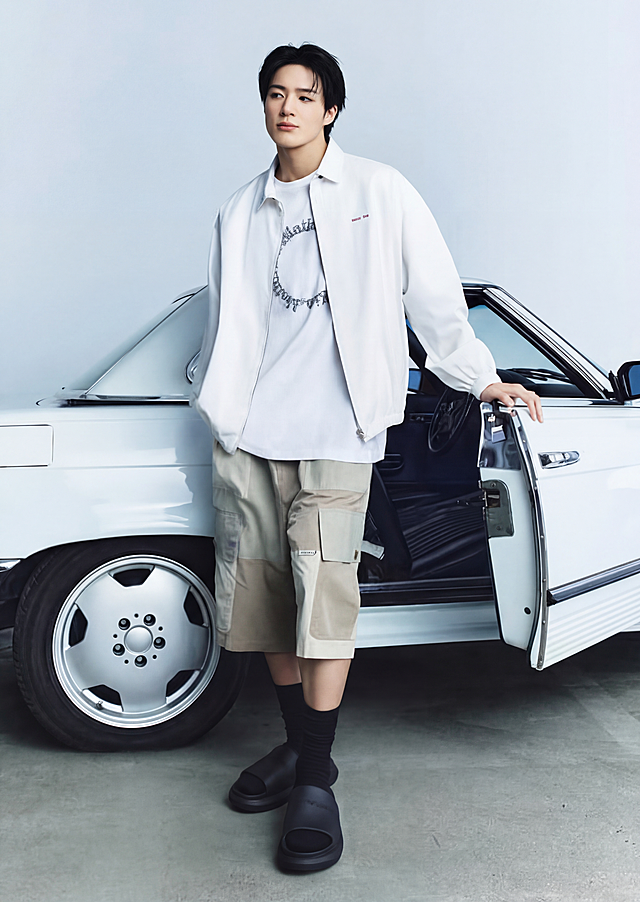 将模特脚上的黑色皮鞋替换为参考图中的黑色厚底拖鞋，高度还原鞋子的品牌压印logo和细节，保持整体光影和风格一致