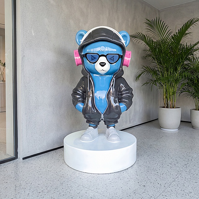 潮流1.7米大熊雕塑，站姿双手插兜姿势保持不变，主体蓝色熊身不变，耳机粉色耳罩不变，将原本紫色连帽套装更换为炭黑色，鞋子保持浅灰色不变，保持整体亮面玻璃钢材质和物理结构绝对不变，严禁扭曲变形。放置在商业展厅入口浅灰色水磨石地面，高级灰肌理墙面展示空间，拉开景深。柔和自然漫射天光，低对比度，阴影极淡柔和，画面明亮干净，营造潮流门店打卡氛围。全景构图，低角度仰拍，展示大熊完整高度。墙角点缀几株大型散尾葵绿植，自然生动。商业级4K，画面通透，严格锁定宽高比为1:1。西方面孔,金发,深眼窝,雀斑,杂乱房间,死黑阴影,硬光,乡村风,高对比度,欧美妆容,变形,扭曲,悬空,比例失调