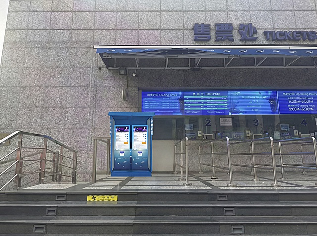 将图2中的旧自助售票机替换为图1的蓝色双屏自助售票机，保持原图中的环境布局、台阶、栏杆、售票处墙面文字和电子屏完全不变，仅替换主体机器。新机器是蓝色双屏自助售票机，带有海洋水母装饰和品牌文字。精准匹配原场景透视角度，实现空间尺度物理融合，确保新产品严丝合缝地嵌入原位置。重置产品光影，增强光照一致性，赋予自然光影及真实接触阴影。产品色温亮度与环境完全协调，增加环境映射。消除视觉接缝，画面自然真实，保持原背景色调，强化真实质感。保持原图比例。4K分辨率。