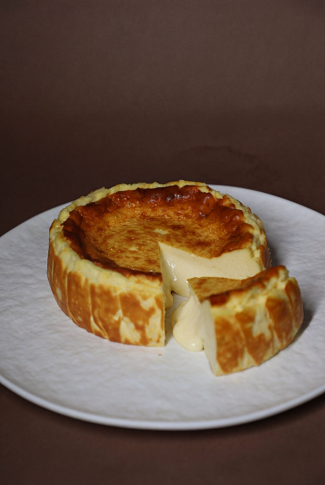 产品摄影工作室照明，俯视角度，超高清，调整巴斯克芝士蛋糕切角，让流心更明显但不要太多，保留蛋糕和背景原有构图和风格