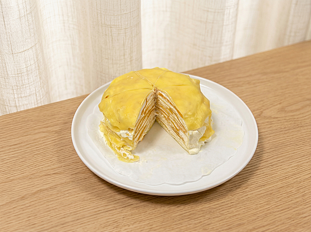 保持千层蛋糕（切开露出多层结构）和白色盘子的物理结构绝对不变，严禁变形。更换为温馨治愈的美食场景：置于浅橡木纹桌面，背景为米白亚麻布帘，柔和漫射光，低对比度莫兰迪暖调，画面干净明亮，商业种草风，4K高清。