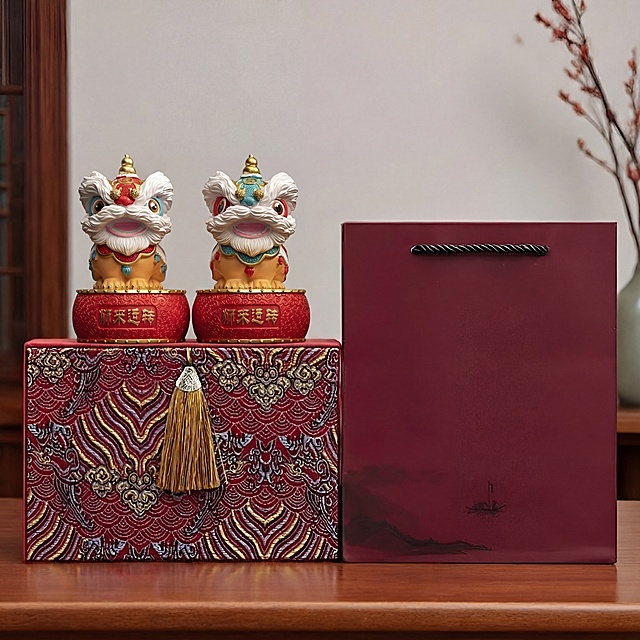将图一中礼盒上原有的两只小狮子完整替换为图二中的两只醒狮小狮子，左侧换红色头部醒狮，右侧换蓝色头部醒狮。
保持两只新狮子完整外观和真实比例，打破原有轮廓束缚，完全覆盖替换。新狮子严格继承原位置的摆放角度、透视关系和底座接触点，稳稳放在原有红色底座上，严禁漂浮偏移变形。仅替换两只狮子，保持图一的红色花纹礼盒、酒红色礼袋、金色流苏、室内背景等所有其他内容完全不变。自然融合边缘，匹配原有光影，严格锁定宽高比1:1，4K高清真实质感。