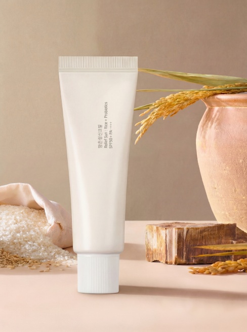 在当前画面基础上，将洗面奶产品等比例放大1.2倍，并向左平移，使其右边缘恰好遮住米白色米口袋的右下角；注意右平移边界不可超过米口袋开口与白色大米接壤的边界线。因左移导致右侧空缺区域，需根据背景中的稻穗预览效果