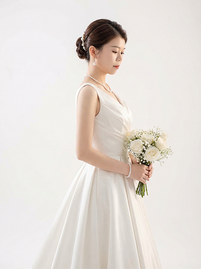 根据图片人物，变换姿态，生成另一张温柔气质新娘，室内极简高级风，白棚简约高级感，纯白色室内场景，高级缎面婚纱，珍珠配饰，柔和柔光，干净高级，极简美学，细腻肤质，杂志风婚纱大片，自然情绪，优雅端庄