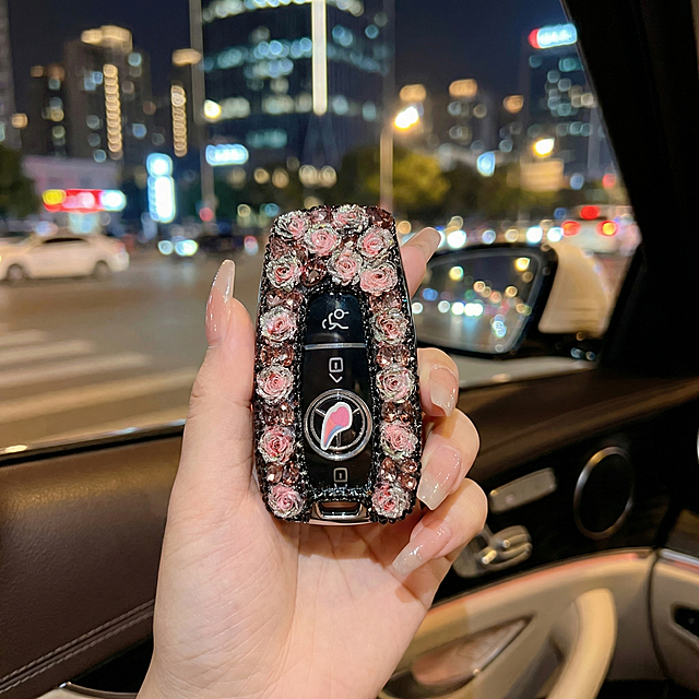 基于原图片修改，保持镶钻玫瑰汽车钥匙扣的产品细节、装饰和结构完全不变，将背景改为车内环境，车外是虚化的大都市夜景，把手修改为修长带有精致美甲的手，整体保持商业种草氛围感，夜景柔和光影，画面通透，产品清晰，保留原图比例。变形,扭曲,穿模,产品结构变形,装饰错位,杂乱,西方面孔,硬光,高对比度