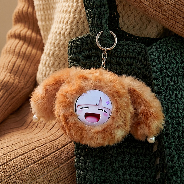 橘色混毛长毛绒挂件，带两只毛绒耳朵，耳朵末端装饰白色珍珠，圆形主体中间带圆形电子表情屏。保持物理结构不变，严禁扭曲拉伸改变产品形态。
深绿色编织包挂饰场景，低饱和度暖调，挂在编织包带上（组合语境）。
柔和全屋漫射柔光。【产品受光面泛起暖米色，暗部及边缘映射深墨绿色的环境光晕。绝对禁止纯白高光，彻底物理融合】。
画面中心特写，聚焦产品主体。自然质感陈列。
微调原平视视角。将纯色桌面替换为深绿色针织包带，背景重构为纹理织物搭配人物手臂，消除原有背景文字。
严格锁定比例 1:1。4K分辨率。变形,扭曲,悬空,比例失调,水印,文字,西方面孔,金发,深眼窝,雀斑,死黑阴影,硬光,高对比度