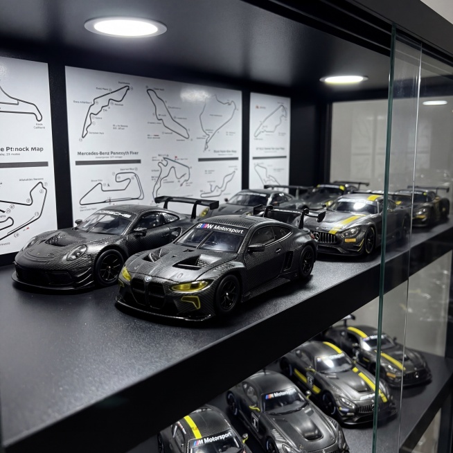 保持原BMW赛车模型的黑色碳纤维纹理、黄色灯组细节、BMW Motorsport标识以及整体物理结构绝对不变，将模型放置在黑色哑光分层玻璃展示柜的中层C位，周围环绕同系列保时捷、奔驰赛车模型，所有模型预览效果