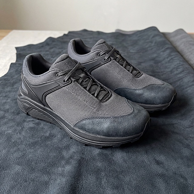 生成一双跑步鞋放在图片提供的深灰皮革上方，鞋头鞋尾处使用该皮革纹路材质，鞋子整体不要只有一个颜色，需搭配另一种不同材质（如透气网面、EVA中底、橡胶外底或TPU支撑片），产品展示场景图，高清真实摄影风格
