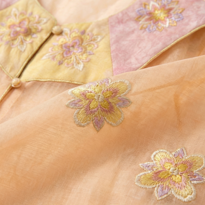 生成这件衣服的面料细节特写图片，重点突出面料的细节、纹理和质感，展现衣服刺绣工艺的精致感，保留原有的浅橘色半透明面料和粉黄撞色刺绣设计，清晰呈现纱质通透感和刺绣肌理，整体自然写实预览效果