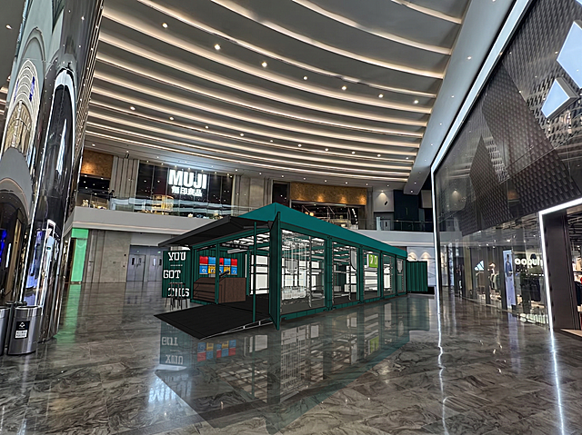 将已经抠出的墨绿色集装箱店铺模型，放到这张商场大厅图片的空白地面居中位置，融合自然，保持真实光影效果，生成一张场景效果图