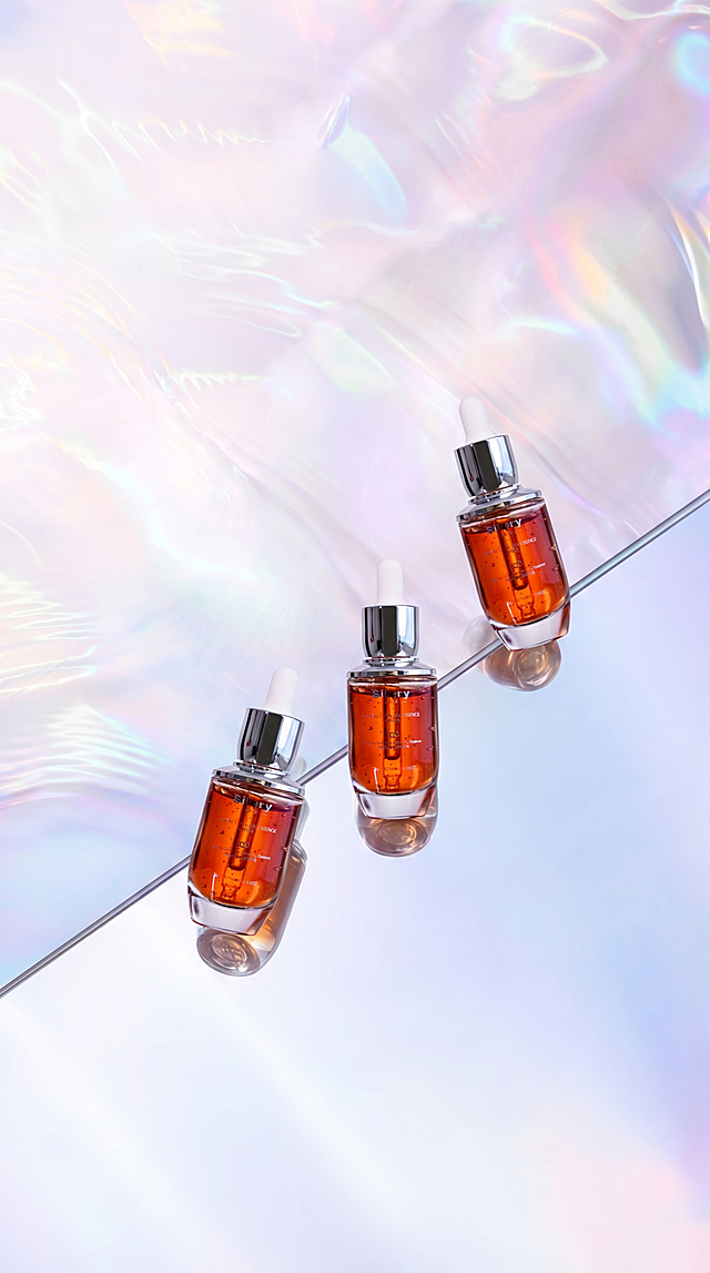 将原图镜面上斜对角排列的三个白色圆柱瓶子原位替换为图2(参考图)中的琥珀色透明玻璃瓶精华液，瓶子带有银色滴管式瓶盖，瓶身有文字标识。
用图2中精华液的真实物理结构完全覆盖该区域，打破原图旧瓶子的轮廓束缚，保持原产品(图2)的真实比例，严禁挤压或变形。新产品需完美继承原图中旧瓶子的摆放角度、镜头高度与透视消失点关系，严格保持旧瓶子的俯视透视效果，并继承旧瓶子的底部接触点，严禁漂浮或位置偏移，使其与背景空间完美融合。仅替换这三个瓶子，保持原图其他环境布局绝对不变。
重置该区域光影，赋予自然接触阴影，完美消除新产品边缘白边，画面自然真实，严格锁定宽高比为 9:16，4K分辨率。