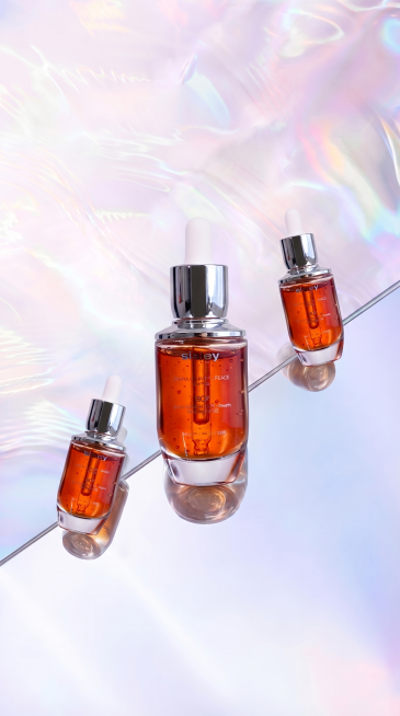 将中间的精华液瓶子适度放大，使其在构图中更突出；同时将左右两侧的瓶子向画面边缘方向轻微平移，保持三瓶呈对角线排列但间距略增，整体仍维持镜面反射与光影一致性。保持产品外观、标签文字、滴管结构完全不变，仅预览效果