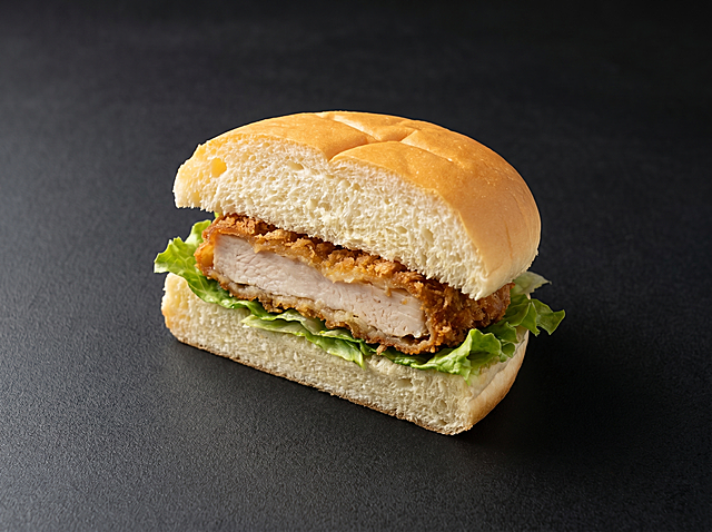 一个单独的鸡排包，采用软质白面包胚（非酥皮/油炸外壳），表面微黄、蓬松柔软，对半切开夹入厚实炸鸡排与新鲜生菜；去除其余所有产品与包装；背景为深灰黑色哑光质感（带细微纹理），左上方柔和侧光增强立体感；高清600*450