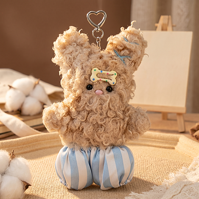 主体是浅卡其色卷毛毛绒兔子挂件，头部带彩色波点骨头发饰，穿蓝白条纹短裤，顶部带有心形金属挂扣。保持物理结构不变，严禁扭曲拉伸改变产品形态。
温馨室内软装场景，暖棕奶油色调，搭配柔和棉絮质感装饰。
柔和侧逆光。【产品受光面泛起暖奶黄色，暗部及边缘映射浅棕米色的环境光晕。绝对禁止纯白高光，彻底物理融合】。
画面居中特写摆放。自然柔和光照，产品悬挂展示。
微调拍摄视角。搭配原木立牌（替换帆布包/线圈本），背景用米色磨砂台面重构细节，消除品牌文字。
严格锁定宽高比为 1:1。4K分辨率