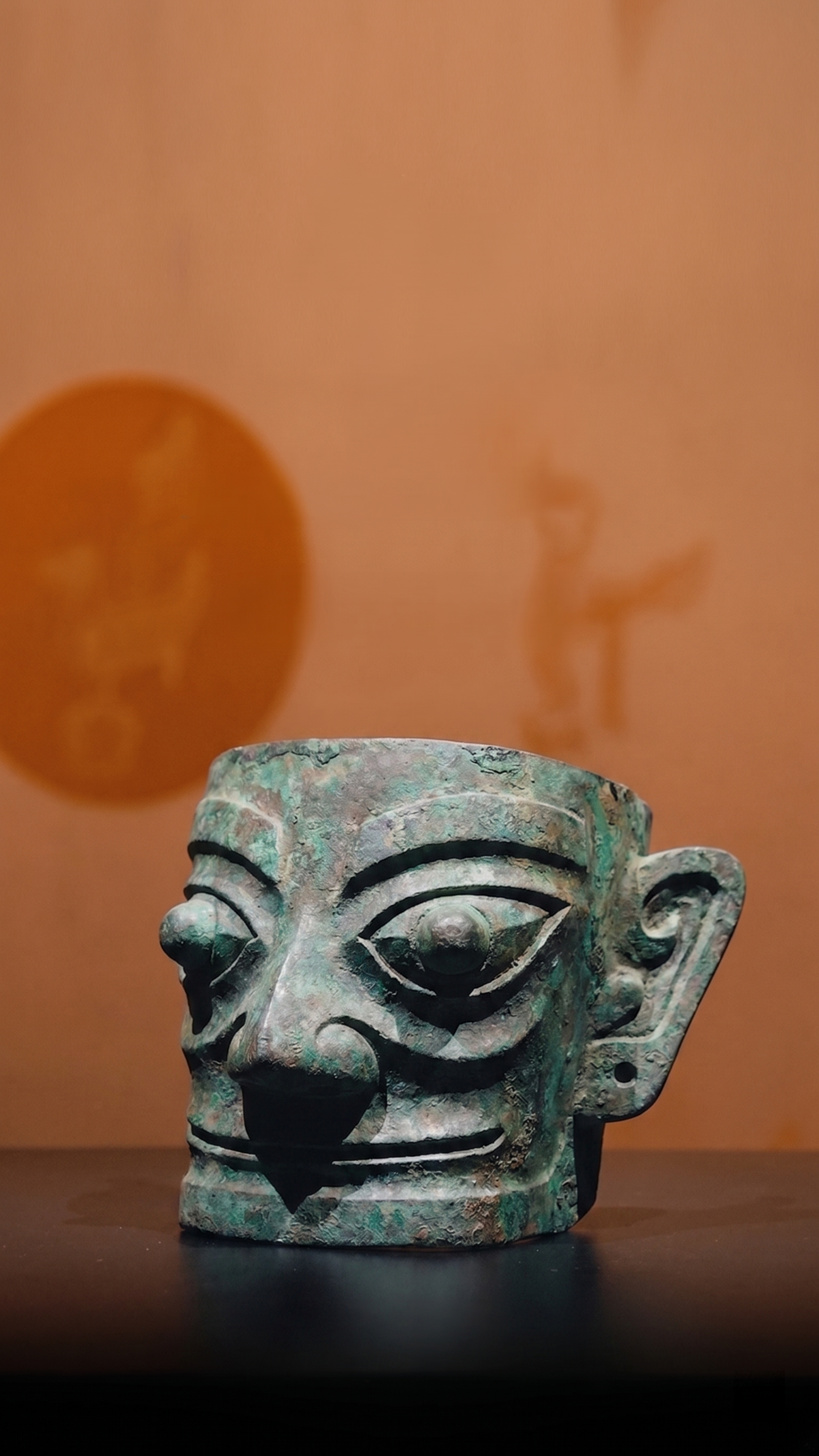 将图中原青铜鸟文物替换为图二的三星堆青铜面具，保持整体构图、光… - 图片创意预览