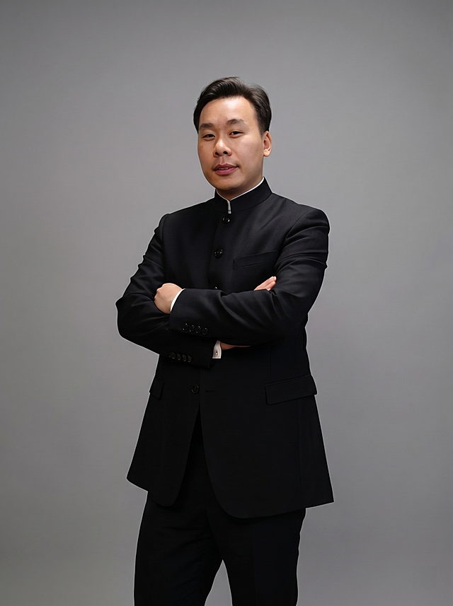 参考图中保留人物脸型、发型、年龄等特征生成职场形象照,标准焦段50mm,f/4光圈(f/2.8-f/4区间),平视视角(镜头与人物视线齐平);人物占画面70%,人物居中(居中构图),位于画面中心,为视觉聚焦点,入境范围头部及以下至臀部下方10cm(半身像);左右留少量背景空间;头部与画面顶部保留5%空间;头部发型完整,头肩比例协调,人物结构准确;身穿黑色立领中山装外套，面料呈细腻微微哑光质感，下装黑色精纺羊毛混纺西裤，着装正式干练，专业稳重，身形匀称，姿态端正，身体挺拔。呈双手抱胸的自然姿态，肢体放松且自信，发质微微柔顺，微微蓬松。简约微微中度灰色纯色背景(呈现均匀柔和质感),背景光线均匀柔和,强化色彩对比的高级感。极简干净;画质超高分辨率、细节清晰,现代精致感风格;肤质精细化处理;眼神直视镜头,目光坚定且澄澈,表情自然自信。嘴角自然。肤质自然细腻,肤色健康均匀,皮肤状态清爽干净,保留真实皮肤细节｡正面柔光补光,4800K中性光,面部光比1:1.5｡中近景写实摄影,对焦清晰,面部雾面柔光,轻透裸肌感,高清保留皮肤细节｡分辨率4K,去除人物之外的所有元素，修整面部下颌，让人物干净清爽自信，严格按照图片内容生成，画面比例3:4。