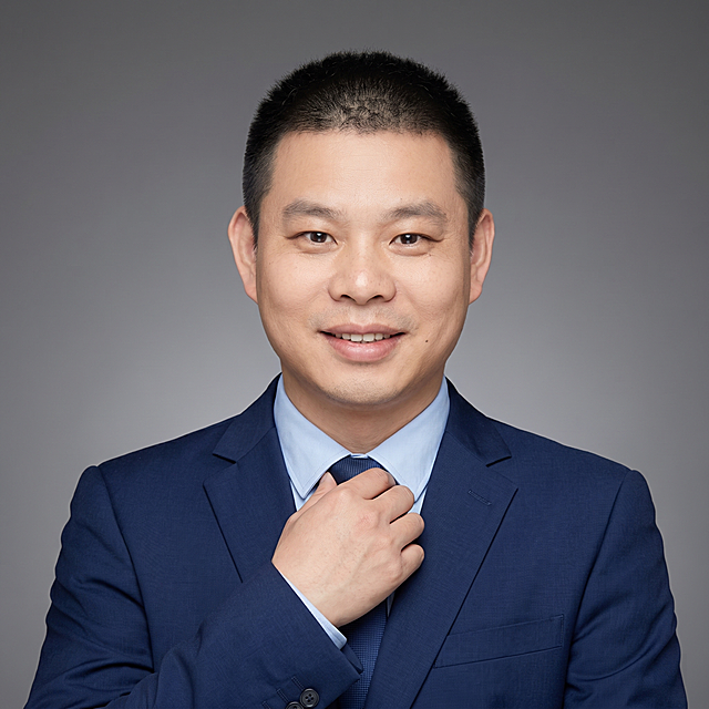 参考图中保留人物脸型、发型、年龄等特征生成销售经理职场大头像形象照，标准焦段50mm，f/4光圈，平视视角，镜头与人物视线齐平；人物占画面70%，人物居中，位于画面中心，为视觉聚焦点，入境范围仅头部及肩部，大头像特写；左右留少量背景空间；头部与画面顶部保留5%空间；头部发型完整，头肩比例协调，人物结构准确；身穿合体商务藏蓝色西装外套，平驳领设计，内搭亮色浅蓝色衬衫，着正式干练，热情有感染力；身形匀称，姿态端正，身体挺拔。呈自然正面站姿，手扶领带，肢体放松且自信；发质微微柔顺，微微蓬松。简约中度灰色渐变背景，呈现均匀柔和质感，背景光线均匀柔和，强化色彩对比的高级感，极简干净；画质超高分辨率、细节清晰，现代精致感风格；肤质精细化处理；眼神直视镜头，目光坚定且澄澈，表情自然，嘴角微微上扬；肤质自然细腻，肤色健康均匀，皮肤状态清爽干净，保留真实皮肤细节。正面柔光补光，4800K中性光，面部光比1:1.5。中近景写实摄影，对焦清晰，面部雾面柔光，轻透裸肌感，高清保留皮肤细节。分辨率4K，去除人物之外的所有元素，严格按照图片内容生成，画面比例1:1