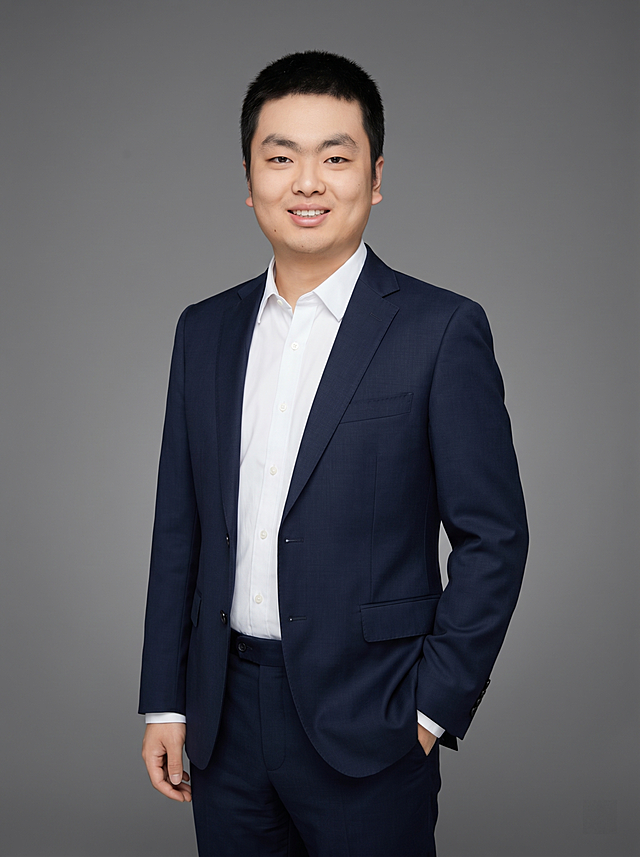 参考图中保留人物脸型、发型、年龄等特征生成职场形象照,标准焦段50mm,f/4光圈(f/2.8-f/4区间),平视视角(镜头与人物视线齐平);人物占画面70%,人物居中(居中构图),位于画面中心,为视觉聚焦点,入境范围头部及以下至臀部下方10cm(半身像);左右留少量背景空间;头部与画面顶部保留5%空间;头部发型完整,头肩比例协调,人物结构准确;发质微微柔顺，微微蓬松。身穿藏青色精纺羊毛混纺西装外套,(平驳领设计,面料呈细腻微微哑光质感);内搭白色高支精梳棉衬衫;下装藏青色精纺羊毛混纺西裤;着装正式干练;专业稳重;身形匀称,姿态端正,身体挺拔。呈左手插兜的自然姿态，肢体放松且自信。简约微微中度灰色纯色背景(呈现均匀柔和质感),背景光线均匀柔和,强化色彩对比的高级感。极简干净;画质超高分辨率、细节清晰,现代精致感风格;肤质精细化处理;眼神直视镜头,目光坚定且澄澈,表情自然。嘴角上扬;肤质自然细腻,肤色健康均匀,皮肤状态清爽干净,保留真实皮肤细节｡正面柔光补光,4800K中性光,面部光比1:1.5｡中近景写实摄影,对焦清晰,面部雾面柔光,轻透裸肌感,高清保留皮肤细节｡分辨率4K,去除人物之外的所有元素。严格按照图片内容生成。画面比例3:4