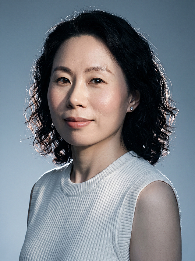 生成高级质感单人写真，仅保留参考图1人物脸型、年龄等特征，忽略参考图中的西装配饰，冷调极简时尚杂志风格，低饱和蓝灰调带有轻微胶片颗粒感，侧光打光形成硬阴影，冷暖对比突出面部明暗层次，发丝自带轮廓光，整体氛围高级清冷；清透奶油肌，真实皮肤纹理，自然气色，乌黑齐肩微卷发，保留原发色；头部微侧，眼神温柔直视镜头，微笑表情自然舒展，肩部放松；妆容干净清透，突出自然骨相，白色竖坑条无袖针织背心，单只简约钻饰耳钉；渐变灰蓝极简纯色背景，无多余杂物；中特写构图，竖幅构图，突出人物面部神态；分辨率4k，电影级光影质感，商业人像摄影级别，画面比例3:4