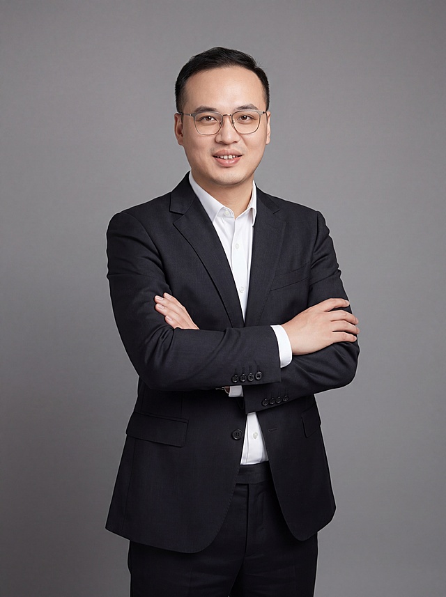 参考图中保留人物脸型、发型、年龄等特征生成职场形象照,标准焦段50mm,f/4光圈(f/2.8-f/4区间),平视视角(镜头与人物视线齐平);人物占画面70%,人物居中(居中构图),位于画面中心,为视觉聚焦点,入境范围头部及以下至臀部下方10cm(半身像);左右留少量背景空间;头部与画面顶部保留5%空间;头部发型完整,头肩比例协调,人物结构准确;发质微微柔顺，微微蓬松。身穿深黑色精纺羊毛混纺西装外套,(平驳领设计,面料呈细腻微微哑光质感);内搭白色高支精梳棉衬衫;下装深黑色精纺羊毛混纺西裤;着装正式干练;专业稳重;身形匀称,姿态端正,身体挺拔。呈双手抱胸的自然姿态，肢体放松且自信;保留佩戴眼镜特征;简约微微中度灰色纯色背景(呈现均匀柔和质感),背景光线均匀柔和,强化色彩对比的高级感。极简干净;画质超高分辨率、细节清晰,现代精致感风格;肤质精细化处理;眼神直视镜头,目光坚定且澄澈,表情自然。嘴角上扬;肤质自然细腻,肤色健康均匀,皮肤状态清爽干净,保留真实皮肤细节｡正面柔光补光,4800K中性光,面部光比1:1.5｡中近景写实摄影,对焦清晰,面部雾面柔光,轻透裸肌感,高清保留皮肤细节｡分辨率4K,去除人物之外的所有元素。严格按照图片内容生成。画面比例3:4