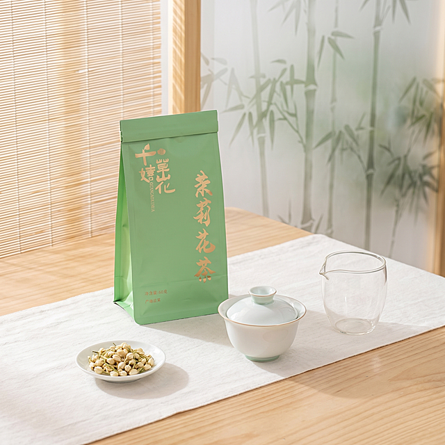 超写实商品场景摄影。
主体：茉莉花茶包装严格参照上传产品图，完整保留所有可见组件、部件、轮廓形状、结构、比例、材质质感、颜色与上传图完全一致，完整保留品牌logo“千草嬉花”、产品名“茉莉花茶”、净含量“60克”信息，杜绝任何变形、色差、组件缺失、结构偏差。产品位于画面核心位置，与茶具呈三角形摆放，背景无其他同类茶产品。
构图：45度俯拍，三角形构图。
风格：清新淡雅，新中式禅意。
场景：新中式茶室，自然光透过竹帘。
空间陈设：①浅色原木茶桌，浅原木纹理；②茶桌中央铺一块白色棉麻茶席；③白色棉麻茶席上，产品包装斜放一侧，旁边放一只白瓷盖碗，另一只玻璃公道杯，呈三角形摆放；④产品包装旁放一小白瓷碟，碟中放少量茉莉干花作为装饰；⑤背景是竹林图案磨砂玻璃隔断，朦胧雅致。
配色：主浅原木色 + 白色 70%，辅产品淡绿色点缀 30%，画面颜色：浅原木色、白色、淡绿色、瓷白色、透明玻璃色。
材质：原木桌面、棉麻茶席、白瓷、玻璃、干花。
光影：主光从前方竹帘透进自然散光，柔和均匀落在桌面；产品和茶具有清晰柔和投影，白瓷有温润高光，玻璃通透轻盈。
窨制茉莉花茶没有茉莉花，却有花香。
去除上传图中的促销文字 / 标签 / 水印 / 排版图层等非产品本体元素，仅保留产品 logo 与必要规格信息。
严格锁定宽高比为 1:1。