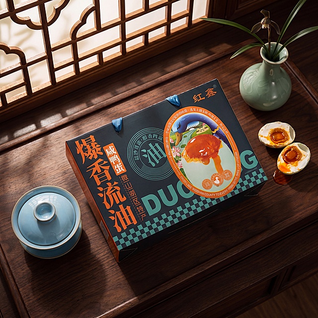 超写实电商产品摄影。
主体：咸鸭蛋礼盒严格参照上传产品图，完整保留所有可见组件、部件、轮廓、结构、比例、材质、颜色与产品本体上的文字信息（logo / 型号 / 规格 / 参数 / 浮雕 / 刻度 / 生产信息等），与上传图完全一致，杜绝变形 / 色差 / 组件缺失 / 文字篡改。产品位于画面黄金位置，完整不裁切，背景无其他同类产品。
构图：中心构图，抬高俯拍。
风格：新中式雅致风。
场景：中式茶桌，古色古香。
承载：①黑胡桃实木茶盘，深棕色实木纹理，哑光质感。
陪衬：①茶盘一侧放汝窑盖碗，天青色釉面；②礼盒旁边放两个剥开的流油咸鸭蛋，油润红亮；③背景处放一个青瓷花瓶，插一枝墨兰。
配色：主深棕 + 黑色 60% / 辅天青 + 墨绿 25% / 点橙红 15%。整体颜色：深棕、黑色、天青、墨绿、橙红。
材质：实木、汝窑陶瓷、青瓷、新鲜鸭蛋。
光影：主光从前方中式木格窗透入暖光，框影斑驳，陶瓷细腻反光，实木纹理柔和。
严格锁定宽高比为 1:1，4K分辨率，产品本体上的文字信息（logo / 型号 / 规格 / 参数 / 浮雕 / 刻度等）100% 保留不变；清除产品本体之外的装饰信息/卖点 / 水印 / 价格 / 排版角标 / 装饰边框等营销信息