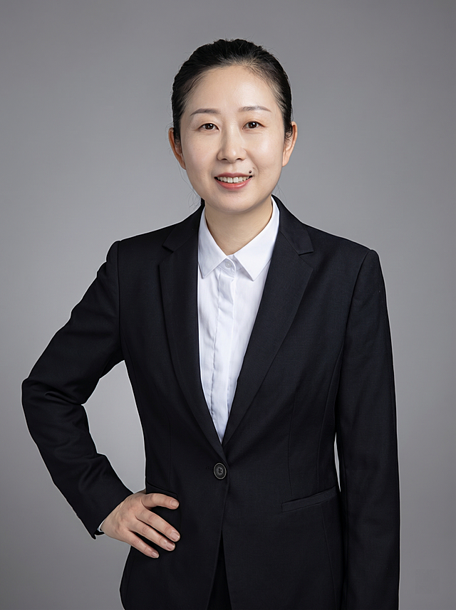 参考图中保留人物脸型、发型、年龄特征生成半身通用职场形象照，保留人物原有黑色西装搭配白色衬衫，保留配饰，人物呈站姿，单手叉腰，肢体放松自信。简约中性灰纯色背景，质感均匀柔和，背景光线均匀，极简干净，画质超高分辨率、细节清晰，现代精致风格，肤质精细化处理，眼神直视镜头，目光坚定，表情自然，画质4K，写实摄影，皮肤质感自然清晰，柔光，正面补光，画面干净清新，高清皮肤细节，肤质自然细腻，肤色均匀，保留真实皮肤细节，画面比例3:4