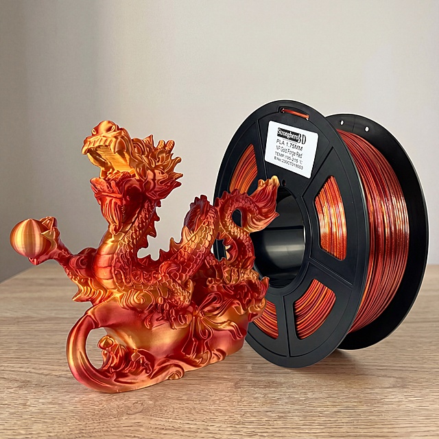 3D打印耗材线轴与中国龙摆件，严格参照上传第一张产品图，完整保留所有可见组件、部件、轮廓、结构、比例、材质、颜色与产品本体上的文字信息，与上传图完全一致。保持产品角度不变，对产品进行精修美化。
场景大类：室内木质桌面，参考图为ins网红居家风格，自然暖色调。
组合语境：产品摆放在木质桌面上，属于3D打印耗材展示场景。
光影：侧前方自然光，产品受光面泛起浅木暖金色，暗部与边缘映射浅灰色光晕，与环境物理融合。
产品位置与构图：居中特写构图。
动态感：静态展示，沉稳自然。
视角微调：微侧15°
全量换款清单：①背景墙面：参考图浅灰白墙面 → 生成图米白色墙面带浅灰光影渐变；②桌面：参考图浅黄原木桌面 → 生成图浅橡木原木桌面，保留木质纹理；③摆件和线轴：保留产品本体结构和角度，优化画质精修。
消除参考图中额外品牌文案，仅保留产品本体原有文字。
4K 分辨率，严格锁定宽高比为 1:1。