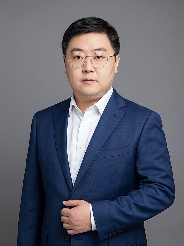 参考图中保留人物脸型、发型、年龄等特征生成金融法律从业者职场形象照，标准焦段50mm，f/4光圈，平视视角（镜头与人物视线齐平）；人物占画面70%，人物居中，居中构图，位于画面中心，为视觉聚焦点，入境范围头部及以下至臀部下方10cm（半身像）；左右留少量背景空间；头部与画面顶部保留5%空间；头部发型完整，头肩比例协调，人物结构准确；发质微微柔顺，微微蓬松。身穿深蓝色精纺羊毛混纺西装外套（平驳领设计，面料呈细腻微微哑光质感）；内搭白色高支精梳棉衬衫；下装深蓝色精纺羊毛混纺西裤；着装正式干练；严谨理性，不怒自威，公信力强；身形匀称，姿态端正，身体挺拔。呈自然站姿，右手轻握西装前襟，肢体放松且自信；佩戴细框眼镜；简约微微中度灰色纯色背景（呈现均匀柔和质感），背景光线均匀柔和，强化色彩对比的高级感，极简干净；画质超高分辨率、细节清晰，现代精致感风格；肤质精细化处理；眼神直视镜头，目光坚定且澄澈，表情自然；肤质自然细腻，肤色健康均匀，皮肤状态清爽干净，保留真实皮肤细节。正面柔光补光，4800K中性光，面部光比1:1.5。中近景写实摄影，对焦清晰，面部雾面柔光，轻透裸肌感，高清保留皮肤细节。分辨率4K，去除人物之外的所有元素。严格按照图片内容生成，画面比例3:4