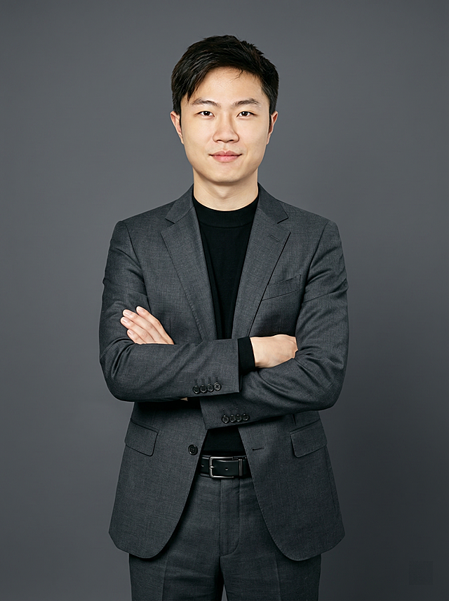 参考图中保留人物脸型、发型、年龄等特征生成职场形象照,标准焦段50mm,f/4光圈(f/2.8-f/4区间),平视视角(镜头与人物视线齐平);人物占画面70%,人物居中(居中构图),位于画面中心,为视觉聚焦点,入境范围头部及以下至臀部下方10cm(半身像);左右留少量背景空间;头部与画面顶部保留5%空间;头部发型完整,头肩比例协调,人物结构准确;发质微微柔顺，微微蓬松。身穿修身精纺羊毛混纺面料的深灰色西装外套(含5%桑蚕丝提升柔光质感),平驳领(商务感正式感),左胸袋无口袋巾(简化高级感),西装下摆自然垂度;内搭黑色中领紧身针织上衣,下装精纺羊毛混纺面料的深灰色高腰直筒西裤(面料同西装),搭配黑色哑光头层牛皮皮带(宽1.5cm),带扣为长方形拉丝黑色金属(1.8cm×2.5cm) ;着装正式干练;正式严谨专业稳重;身形匀称,姿态端正,身体挺拔。呈正面抱胸的自然站立姿态:左臂搭于右臂上方,肩颈自然松弛下沉,姿态自信从容;简约冷调深灰色纯色背景(呈现均匀柔和质感),背景光线均匀柔和,强化色彩对比的高级感。极简干净;画质超高分辨率、细节清晰,现代精致感风格;肤质精细化处理;眼神直视镜头,目光坚定且澄澈,表情自然。嘴角上扬;肤质自然细腻,肤色健康均匀,皮肤状态清爽干净,保留真实皮肤细节｡正面柔光补光,4800K中性光,面部光比1:1.5｡中近景写实摄影,对焦清晰,面部雾面柔光,轻透裸肌感,高清保留皮肤细节｡分辨率4K,去除人物之外的所有元素。严格按照图片内容生成。画面比例3:4