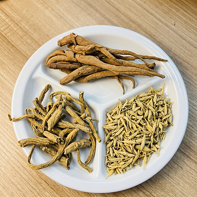 三种中药材分别是：顶部新上传图片的甜当归、左下方西藏党参、右下方麦冬，甜当归严格参照新上传产品图，党参和麦冬保留原形态，完整保留所有可见组件、轮廓形状、结构、比例、材质质感、颜色，与对应上传图完全一致。
画面中无任何文字标注和表述。
室内木质桌面，暖棕自然色调。
圆形白色陶瓷碟子承载三种中药材，顶部放置甜当归，左下方放置西藏党参，右下方放置麦冬，保留参考图产品位置，三个产品之间留有合理空间，不发生穿模遮挡。
斜侧顶光（还原参考图光影方向），产品受光面泛起暖棕木色，暗部映射浅棕木纹光晕，与环境物理融合。
居中构图，微侧20度视角。
背景：保留浅木色桌面背景，保留整体色调与光影位置。
4K分辨率，严格锁定宽高比为1:1。