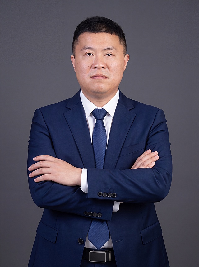 参考图中保留人物脸型、发型、年龄等特征生成职场形象照，标准焦段50mm,F/4光圈(处于F/2.8-F/4区间),平视视角(镜头与人物视线齐平);人物占画面70%,人物居中(居中构图),位于画面中心,为视觉聚焦点,入境范围头部及以下至臀部下方10cm(半身像)构图，身形匀称,姿态端正;身穿精纺羊毛混纺面料的深墨蓝色西装外套(含5%桑蚕丝提升柔光质感),平驳领设计增加商务感正式感,左胸袋无口袋巾简化呈现高级感,西装下摆自然垂度;内搭长绒棉白色衬衫(温莎领),袖口贴合手腕1cm无堆叠;搭配精致且高级的深蓝色斜向微微渐隐光泽感极细条纹商务感领带(丝提花材质,低饱和柔光渐隐);下装精纺羊毛混纺面料的深墨蓝色高腰直筒西裤(面料同西装);搭配黑色哑光头层牛皮皮带(宽2.5cm),带扣为长方形拉丝黑色金属(1.8cm×3cm) ;呈正面抱胸的自然站立姿态:左臂搭于右臂上方,肩颈自然松弛下沉,姿态自信从容,正式严谨专业稳重;发梢微微修整,干练大气;背景光线均匀柔和,强化色彩对比的高级感。简约冷调深灰色纯色背景(呈现均匀柔和质感),极简干净 背景;画质超高分辨率、细节清晰,现代精致感风格;肤质精细化处理;眼神直视镜头,目光坚定且澄澈,表情自然;肤质自然细腻,肤色健康均匀,哑光肤质清爽干净,保留真实皮肤细节;杰作,最佳画质,超高细节,写实摄影,中近景人像,皮肤质感自然清晰,柔光,正面补光,画面干净清新,高清皮肤细节;面部光比1:1.5,4800K中性光,微微修饰脸型,肤质哑光细腻,面部雾面柔光,轻透裸肌感,真实毛孔纹理;分辨率4K,严格按照图片内容生成,画面比例3:4