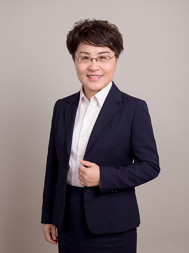参考图中保留人物脸型、发型、年龄等特征生成职场形象照,标准焦段50mm,f/4光圈(f/2.8-f/4区间),平视视角(镜头与人物视线齐平);人物占画面70%,人物居中(居中构图),位于画面中心,为视觉聚焦点,入境范围头部及以下至臀部下方10cm(半身像);左右留少量背景空间;头部与画面顶部保留5%空间;头部发型完整,头肩比例协调,人物结构准确;发质微微柔顺，微微蓬松。身穿藏青色精纺羊毛混纺西装外套,(平驳领设计,面料呈细腻微微哑光质感);内搭白色高支精梳棉衬衫;下装藏青色精纺羊毛混纺西装套裙;着装正式干练;严谨理性、值得信赖;身形匀称,姿态端正,身体挺拔。呈右手轻握西装前襟的自然姿态，肢体放松且自信;佩戴精致眼镜配饰。简约微微暖调暖灰纯色背景(呈现均匀柔和质感),背景光线均匀柔和,强化色彩对比的高级感,极简干净;画质超高分辨率、细节清晰,现代精致感风格;肤质精细化处理;眼神直视镜头,目光坚定且澄澈,表情自然。嘴角上扬;清透自然裸妆(轻薄底妆+淡唇妆)妆感轻薄轻透裸肌感,通透感肤质,肤质自然细腻,肤色健康均匀,雾面柔光裸肌感,保留真实皮肤细节｡正面柔光补光,4800K中性光,面部光比1:1.5,色调明亮｡中近景写实摄影,对焦清晰,高清保留皮肤细节｡分辨率4K,去除人物之外的所有元素。严格按照图片内容生成。画面比例3:4