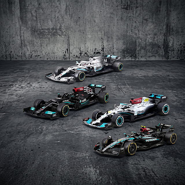 F1赛车模型，严格参照上传产品图（image1），完整保留所有可见组件、部件、轮廓形状、结构、比例、材质质感、颜色与产品本体上的文字信息，与上传图完全一致。
室外水泥地面场景，自然灰调工业风色调。
保留参考图（image2）骨架：承载面为水泥地面、背景为水泥墙面，整体排布方式与光影氛围一致。侧前方自然光，产品受光面泛起水泥灰色、暗部映射浅灰光晕，与环境物理融合。
产品居中展示，保持所有四辆赛车组合排布，微俯视角相对参考图偏转20度。
全量换款清单：
①背景墙面：参考图浅灰色水泥墙 → 生成图深灰色做旧水泥墙，同水泥材质换纹理色调
②地面：参考图浅灰色水泥地 → 生成图深灰色斑驳水泥地，同水泥材质换纹理
③其他赛车：参考图其他车队赛车 → 保留数量和位置，仅为同材质换不同车队款式，保持赛车品类
相似度50%，保留图1商品外观颜色不变，实物拍摄展示，消除品牌文字之外的多余信息。
4K 分辨率，严格锁定宽高比为 1:1