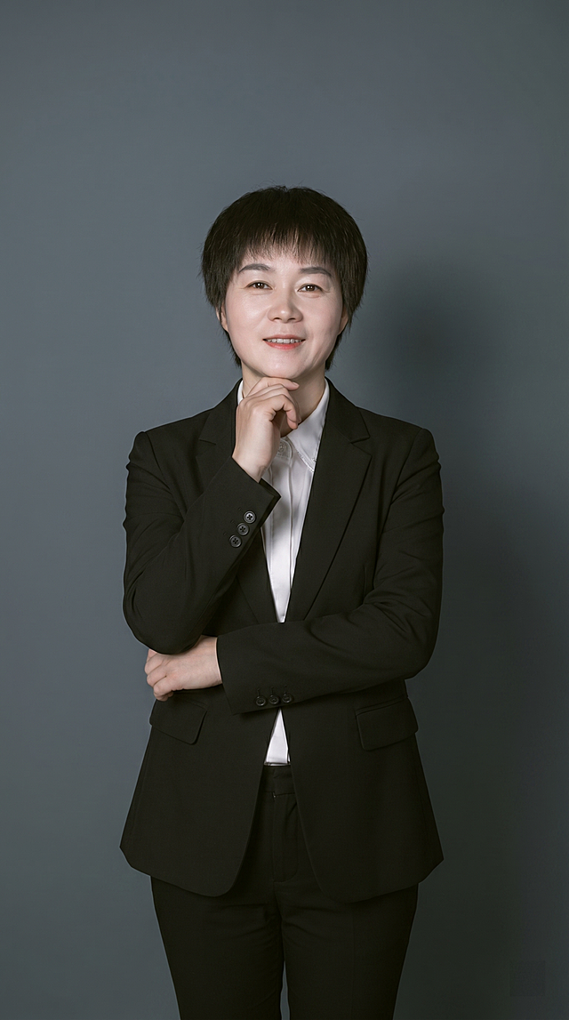 参考图中保留人物脸型、发型、年龄等特征生成职场形象照,标准焦段50mm,f/4光圈(f/2.8-f/4区间),平视视角(镜头与人物视线齐平);人物占画面70%,人物居中(居中构图),位于画面中心,为视觉聚焦点,入境范围头部及以下至臀部下方10cm(半身像);身穿黑色亚面精纺面料西装外套;内搭白色衬衫;下装黑色亚面精纺面料西裤;着装正式干练;专业稳重;身形匀称,姿态端正,身体挺拔。左手手轻托下颌;右手自然交叉于臂弯,身姿随性有度,自然松弛姿势,肢体放松且自信;发梢微微修整,干练大气,主体锐利,背景光线均匀柔和,强化色彩对比的高级感。简约冷调深灰色纯色背景(呈现均匀柔和质感),极简干净;画质超高分辨率、细节清晰,现代精致感风格;肤质精细化处理;眼神直视镜头,目光坚定且澄澈,表情自然。嘴角上扬;肤质自然细腻,肤色健康均匀,哑光肤质清爽干净,保留真实皮肤细节;杰作,最佳画质,超高细节,写实摄影,中近景人像,皮肤质感自然清晰,柔光,正面补光,画面干净清新,高清皮肤细节;面部光比1:1.5,4800K中性光,微微修饰脸型,肤质哑光细腻,面部雾面柔光,轻透裸肌感,真实毛孔纹理;分辨率4K,严格按照图片内容生成,画面比例9:16