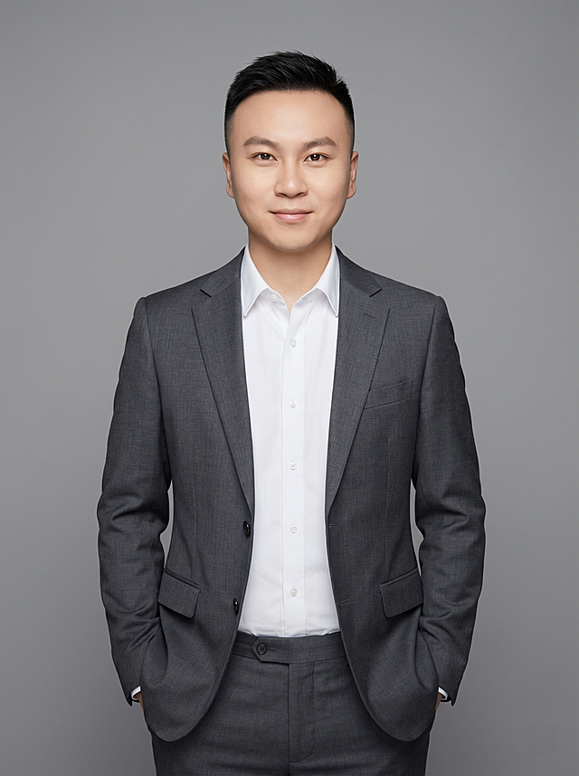 参考图中保留人物脸型、发型、年龄等特征生成职场形象照，标准焦段50mm，f/4光圈，平视视角，镜头与人物视线齐平；人物占画面70%，人物居中，居中构图，位于画面中心，为视觉聚焦点，入境范围头部及以下至臀部下方10cm，半身像；左右留少量背景空间；头部与画面顶部保留5%空间；头部发型完整，头肩比例协调，人物结构准确；发质微微柔顺，微微蓬松。身穿炭灰色精纺羊毛混纺西装外套，平驳领设计，面料呈细腻微微哑光质感；内搭白色高支棉衬衫；下装炭灰色精纺羊毛混纺西裤；着装正式干练；专业稳重，身形匀称，姿态端正，身体挺拔。呈双手插兜的自然站姿，肢体放松且自信。简约微微中度灰色纯色背景，呈现均匀柔和质感，背景光线均匀柔和，强化色彩对比的高级感，极简干净。画质超高分辨率、细节清晰，现代精致感风格；肤质精细化处理；眼神直视镜头，目光坚定且澄澈，表情自然。嘴角上扬；肤质自然细腻，肤色健康均匀，皮肤状态清爽干净，保留真实皮肤细节｡正面柔光补光，4800K中性光，面部光比1:1.5｡中近景写实摄影，对焦清晰，面部雾面柔光，轻透裸肌感，高清保留皮肤细节｡分辨率4K，去除人物之外的所有元素。严格按照图片内容生成。画面比例3:4
