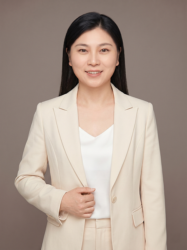 参考图中保留人物脸型、年龄、发型（黑色顺直长发）等特征生成职场形象照，暖灰色暖调背景，乳白色低饱和度西装外套；标准焦段50mm，f/4光圈(f/2.8-f/4区间)，平视视角(镜头与人物视线齐平)；人物占画面70%，人物居中(居中构图)，位于画面中心，为视觉聚焦点;入境范围头部及以下至臀部下方10cm(半身像)；左右留少量背景空间；头部与画面顶部保留5%空间；头部发型完整，头肩比例协调，人物结构准确；发质微微柔顺顺直;身穿低饱和度乳白色精纺羊毛混纺西装外套，柔和低饱和色调，(平驳领设计，面料呈细腻微微哑光质感)；内搭白色真丝吊带背心（无袖，V领，简约修身）；下装同色系精纺羊毛混纺西裤；着装正式干练且具现代感；专业温和；身形匀称，姿态端正，身体挺拔。呈自然站姿，右手轻握西装前襟，肢体放松且自信；简约暖灰色暖调纯色背景(呈现均匀柔和质感)，背景光线均匀柔和，强化色彩对比的高级感。极简干净；画质超高分辨率、细节清晰，现代精致感风格；肤质精细化处理；眼神直视镜头，目光坚定且澄澈，表情自然。嘴角上扬；清透自然裸妆(轻薄底妆+淡唇妆)，妆感轻薄轻透裸肌感，通透感肤质，肤质自然细腻，肤色健康均匀，雾面柔光裸肌感，保留真实皮肤细节｡正面柔光补光，4800K暖调，面部光比1:1.5，色调明亮｡中近景写实摄影，对焦清晰;分辨率4K，去除人物之外的所有元素。严格按照图片内容生成。画面比例3:4