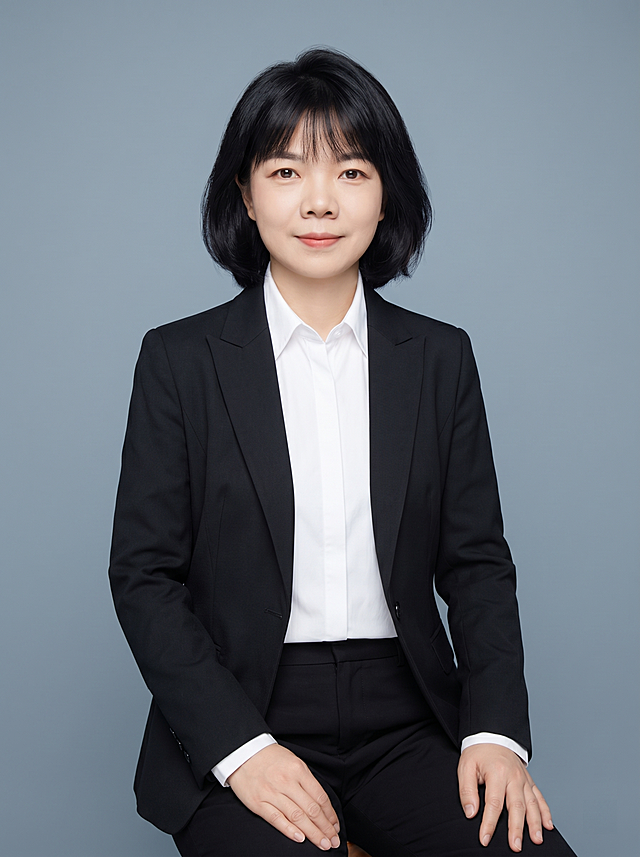 参考图中保留人物脸型、发型、年龄等特征生成律师职场形象照,标准焦段50mm,f/4光圈(f/2.8-f/4区间),平视视角(镜头与人物视线齐平);人物占画面70%,人物居中(居中构图),位于画面中心,为视觉聚焦点,入境范围头部及以下至臀部下方10cm(半身像);左右留少量背景空间;头部与画面顶部保留5%空间;头部发型完整,头肩比例协调,人物结构准确;发质微微柔顺，微微蓬松。身穿黑色精纺羊毛混纺正装西装外套,(平驳领设计,面料呈细腻微微哑光质感);内搭白色高支精梳棉长袖衬衫;下装黑色干练九分西装裤;着装正式干练;严谨理性，逻辑清晰;身形匀称,姿态端正,身体挺拔。呈自然坐姿，双手自然放置，肢体放松且自信;去除原有徽章配饰。简约微微冷灰蓝纯色背景(呈现均匀柔和质感),背景光线均匀柔和,强化色彩对比的高级感，极简干净;画质超高分辨率、细节清晰,现代精致感风格;肤质精细化处理;眼神直视镜头,目光坚定且澄澈,表情自然。嘴角上扬;清透自然裸妆(轻薄底妆+淡唇妆)妆感轻薄轻透裸肌感,通透感肤质,肤质自然细腻,肤色健康均匀,雾面柔光裸肌感,保留真实皮肤细节｡正面柔光补光,4800K中性光,面部光比1:1.5,色调明亮｡中近景写实摄影,对焦清晰,高清保留皮肤细节｡分辨率4K,去除人物之外的所有元素。严格按照图片内容生成。画面比例3:4