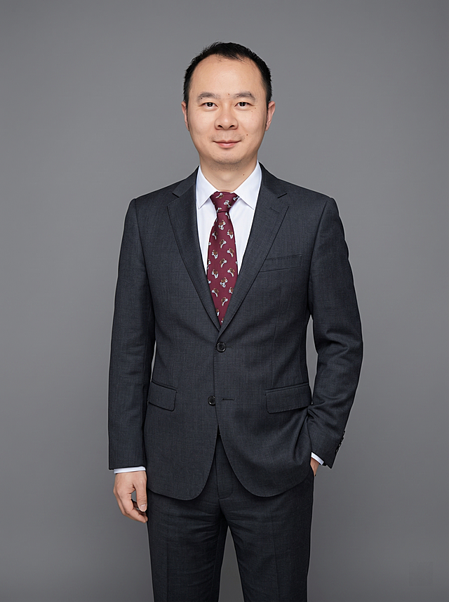参考图中保留人物脸型、发型、年龄等特征生成通用职场正装全身形象照，标准焦段50mm，f/4光圈，平视视角，镜头与人物视线齐平；人物占画面合适比例，人物居中，居中构图，位于画面中心，为视觉聚焦点，全身照，展现人物完整身形；左右留少量背景空间；头部与画面顶部保留合理空间；头部发型完整，头身比例协调，人物结构准确；身穿深灰色精纺羊毛混纺西装外套，平驳领设计，面料呈细腻微微哑光质感；内搭白色高支精梳棉衬衫；下装深灰色精纺羊毛混纺西裤；着装正式干练，专业稳重；身形匀称，姿态端正，身体挺拔。呈单手插兜的自然站姿，肢体放松且自信；佩戴藏青色领带，保留领带配饰；发质微微柔顺，微微蓬松。简约微微中度灰色纯色背景，呈现均匀柔和质感，背景光线均匀柔和，强化色彩对比的高级感，极简干净；画质超高分辨率、细节清晰，现代精致感风格；肤质精细化处理；眼神直视镜头，目光坚定且澄澈，表情自然。嘴角上扬；肤质自然细腻，肤色健康均匀，皮肤状态清爽干净，保留真实皮肤细节｡正面柔光补光，4800K中性光，面部光比1:1.5｡写实摄影，对焦清晰，面部雾面柔光，轻透裸肌感，高清保留皮肤细节；分辨率4K，去除人物之外的所有元素，严格按照图片内容生成，画面比例3:4