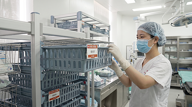 基于原图保留货架、浅蓝色塑料篮子及标签信息不变，增加一位中国女医护人员，戴着口罩和无菌手套，单手正在拉出这个抽拉式浅蓝色塑料篮子，背景为医院手术室或药房环境，整体专业干净。严格锁定宽高比为 16:9