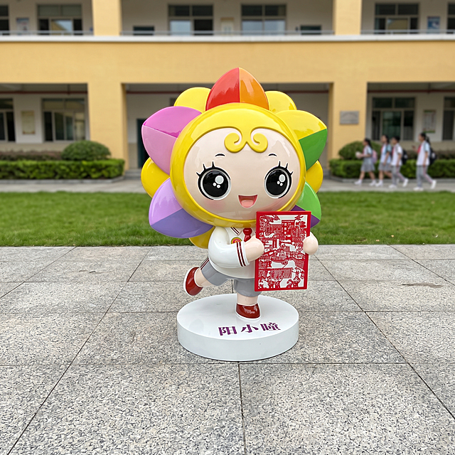 超写实学校校园场景摄影。
主体：雕塑摆件严格参照上传产品图，完整保留所有可见组件、轮廓、结构、比例、材质、颜色与产品本体上的文字信息（“阳小瞳”、logo等），完整保留表面光滑釉面纹理和手作雕塑质感。产品占画面70%，完整不裁切，近景拍摄，保留底座上完整的“阳小瞳”文字。底座稳定放置在学校广场地面，整体与场景光影自然融合，处于同一物理空间。
构图：中心对称构图，平视角度。
风格：校园文创真实摄影。
场景：学校入口广场落地摆件，明亮户外校园环境，背景是教学楼和绿化草坪，充满青春校园氛围。
空间：① 产品放置在浅灰色石材广场地面；② 背景远处，暖黄色教学楼墙面；③ 教学楼前方，绿色草坪与灌木绿植；④ 远景少量模糊学生轮廓。
配色 / 材质：浅灰 / 暖黄 / 彩色 / 绿色；石材 / 涂料 / 草坪 / 玻璃钢雕塑亮面；颜色总数不超过5种。
光影：主光从斜前方45度照射，明亮自然光，清晰展示雕塑亮面反光和校园环境，阴影柔和自然。
参数：4K写实。严格锁定宽高比为1:1。