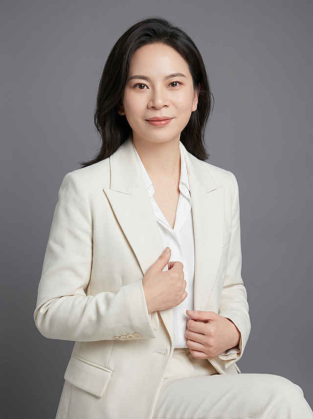 参考图中保留人物脸型、发型、年龄等特征生成职场形象照,标准焦段50mm,f/4光圈(f/2.8-f/4区间),平视视角(镜头与人物视线齐平);人物占画面70%,人物居中(居中构图),位于画面中心,为视觉聚焦点,入境范围头部及以下至臀部下方10cm(半身像);左右留少量背景空间;头部与画面顶部保留5%空间;头部发型完整,头肩比例协调,人物结构准确;发质微微柔顺，微微蓬松。身穿米白精纺羊毛混纺西装外套,(平驳领设计,面料呈细腻微微哑光质感);内搭白色衬衫;下装米白精纺羊毛混纺九分西装裤;着装正式干练;端庄亲和、严谨理性;身形匀称,姿态端正,身体挺拔。呈右手轻握西装前襟的自然姿态，肢体放松且自信;简约微微中度灰色纯色背景(呈现均匀柔和质感),背景光线均匀柔和,强化色彩对比的高级感。极简干净;画质超高分辨率、细节清晰,现代精致感风格;肤质精细化处理;眼神直视镜头,目光坚定且澄澈,表情自然。嘴角上扬;清透自然裸妆(轻薄底妆+淡唇妆)妆感轻薄轻透裸肌感,通透感肤质,肤质自然细腻,肤色健康均匀,雾面柔光裸肌感,保留真实皮肤细节｡正面柔光补光,4800K中性光,面部光比1:1.5,色调明亮｡中近景写实摄影,对焦清晰,高清保留皮肤细节｡分辨率4K,去除人物之外的所有元素。严格按照图片内容生成。画面比例3:4