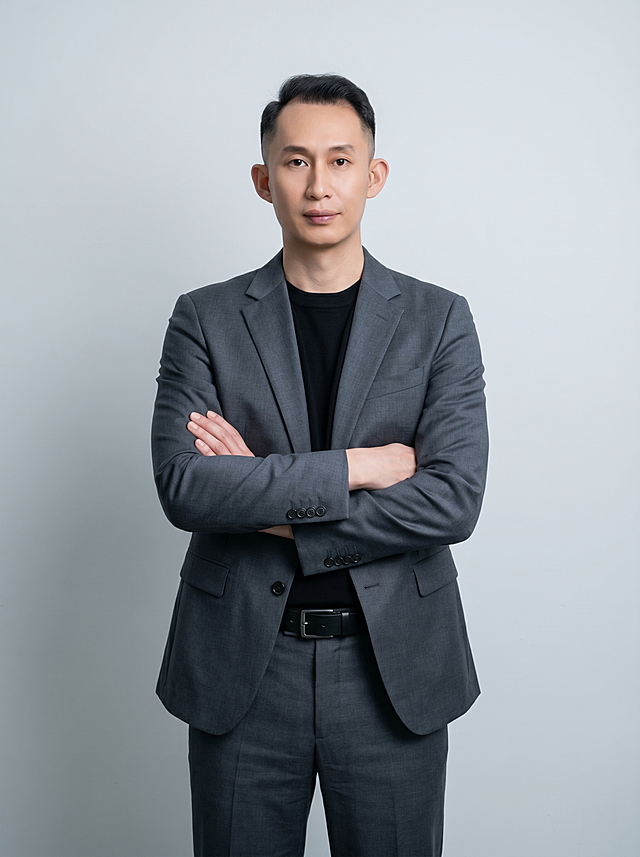 参考图中保留人物脸型、发型、年龄等特征生成职场形象照，标准焦段50mm,F/4光圈(处于F/2.8-F/4区间),平视视角(镜头与人物视线齐平);人物占画面70%,人物居中(居中构图),位于画面中心,为视觉聚焦点,入境范围头部及以下至臀部下方10cm(半身像)构图；身穿修身精纺羊毛混纺面料的深灰色西装外套(含5%桑蚕丝提升柔光质感),平驳领(商务感正式感),左胸袋无口袋巾(简化高级感),西装下摆自然垂度;内搭黑色中领紧身针织上衣,下装精纺羊毛混纺面料的深灰色高腰直筒西裤(面料同西装),搭配黑色哑光头层牛皮皮带(宽1.5cm),带扣为长方形拉丝黑色金属(1.8cm×2.5cm);着装正式干练;正式严谨专业稳重;身形匀称,姿态端正，身体挺拔。呈正面抱胸的自然站立姿态:左臂搭于右臂上方,肩颈自然松弛下沉,姿态自信从容；发梢微微修整,干练大气,主体锐利;简约冷调浅灰色纯色背景(呈现均匀柔和质感),背景光线均匀柔和,强化色彩对比的高级感,极简干净背景；画质超高分辨率、细节清晰,现代精致感风格;肤质精细化处理;眼神直视镜头,目光坚定且澄澈,表情自然；肤色健康均匀,哑光肤质清爽干净,保留真实皮肤细节;杰作,最佳画质,超高细节,写实摄影,中近景人像,皮肤质感自然清晰,柔光,正面补光,画面干净清新,高清皮肤细节;面部光比1:1.5,4800K中性光,微微修饰脸型,肤质哑光细腻,面部雾面柔光,轻透裸肌感,真实毛孔纹理;分辨率4K,严格按照图片内容生成,画面比例3:4